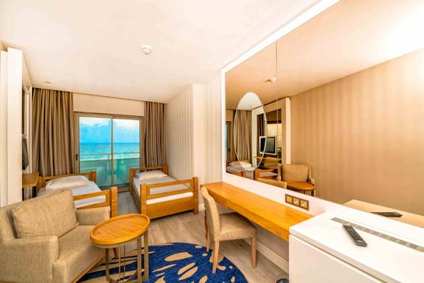 Hotelzimmer von Sidemarin Kirman Premium mit zwei Betten, einem Schreibtisch und einem großen Spiegel, der einen Blick auf das Meer bietet.
