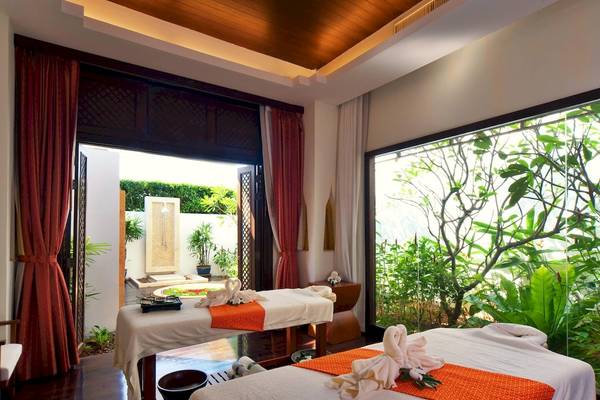 Massageraum im JW Marriott Khao Lak Resort & Spa mit zwei Betten, roten Vorhängen und Glaswänden.