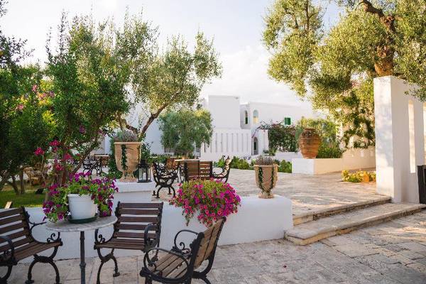 Gartenbereich des Il Melograno Hotels mit Bäumen, Bänken und Tischen.