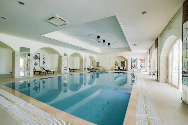 Innenpool des Hotels Il Melograno mit weißen Fliesen und Lounge-Bereichen.
