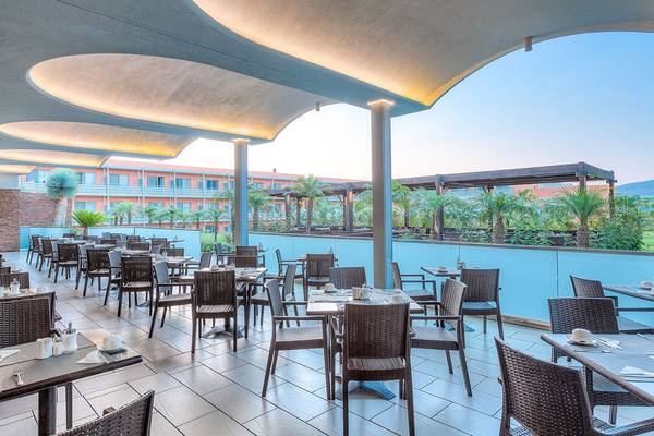 Innenansicht des Restaurants des Blue Lagoon Resorts mit Tischen und Stühlen, umgeben von Pflanzen und Gebäuden.
