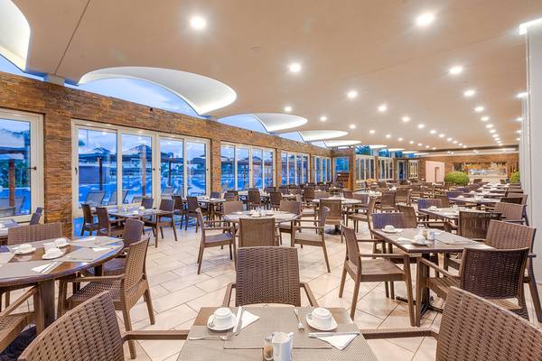 Innenansicht des Restaurants im Blue Lagoon Resort mit runden Tischen und Stühlen, großen Fenstern und Blick auf den Pool.
