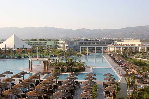 Luftaufnahme des Blue Lagoon Resorts mit großen Swimmingpools, Sonnenschirmen und Liegestühlen vor bergiger Kulisse