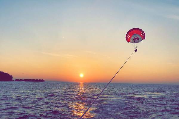 Zwei Personen parasailing bei Sonnenuntergang am Fihalhohi Island Resort.