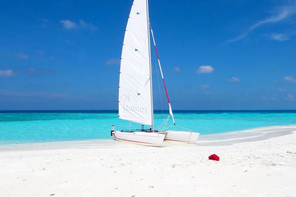Ein Segelboot steht am Strand des Fihalhohi Island Resorts mit kristallklarem Wasser und weißem Sand.