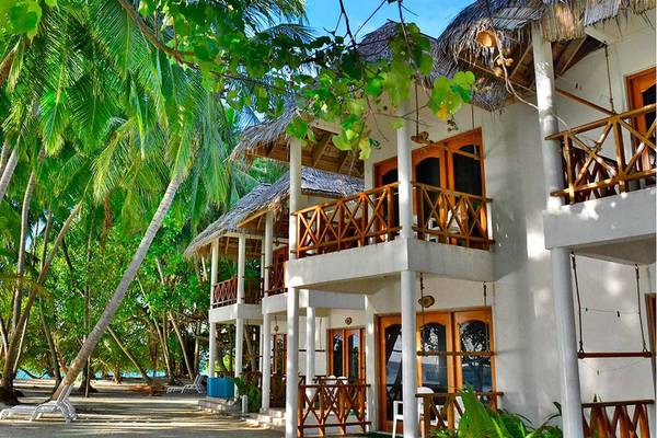 Außenansicht des Fihalhohi Island Resorts mit weißen Villen, Holzbalkonen und Palmen.