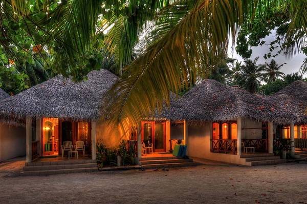 Fihalhohi Island Resort Hütten bei Abendstimmung mit warmem Licht und umgeben von Palmen