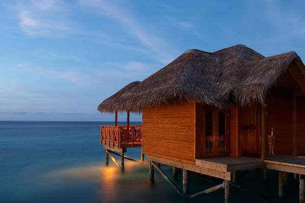 Wasserbungalows des Fihalhohi Island Resorts bei Sonnenuntergang mit Blick auf das Meer