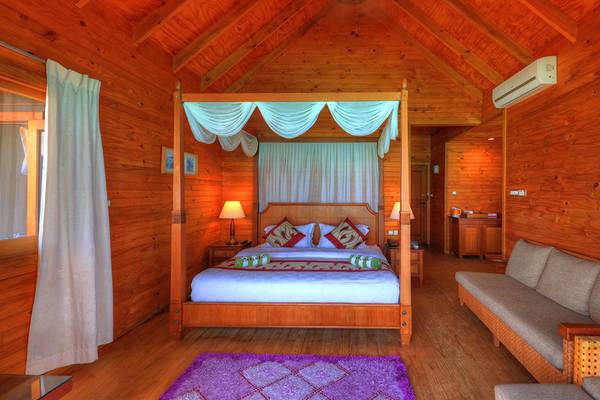 Innenansicht des Schlafzimmers im Fihalhohi Island Resort mit vierpfostenbett, Couch, Teppich und Holzwand.