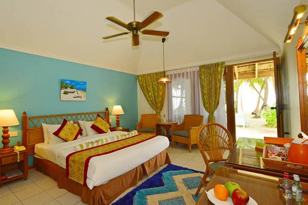 Schlafzimmer im Fihalhohi Island Resort mit blauen Wänden, einem großen Bett, Deckenventilator, Nachttischen mit Lampen und einem offenen Eingang zur Terrasse.
