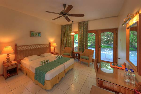 Doppelzimmer im Fihalhohi Island Resort mit zwei Betten, Deckenventilator, Lampen, Stühlen, Glastüren und Spiegel.