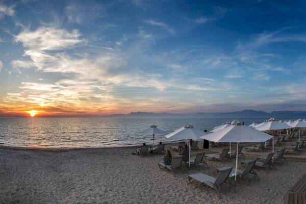 Sonnenuntergang am Strand des Acharavi Beach Hotel mit vielen Sonnenschirmen und Liegestühlen.