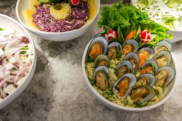 Drei Schüsseln mit verschiedenen Gerichten auf Eis, darunter eine mit Muscheln, Salat und Reis.