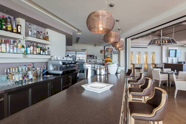 Innenansicht der Bar im Acharavi Beach Hotel mit langen Theke, Stühlen und Flaschen.