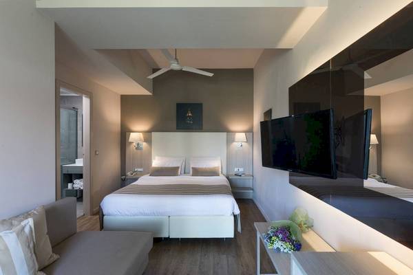 Innenansicht eines Hotelzimmers mit einem großen Bett, Fernseher und einem Spiegel im Acharavi Beach Hotel.