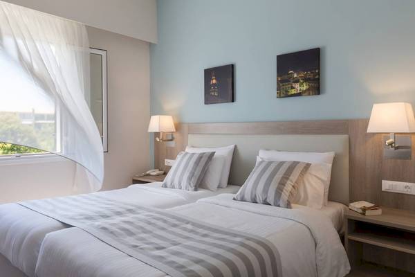 Doppelzimmer im Acharavi Beach Hotel mit zwei Betten, Nachttischen und Stadtbildern an der Wand.
