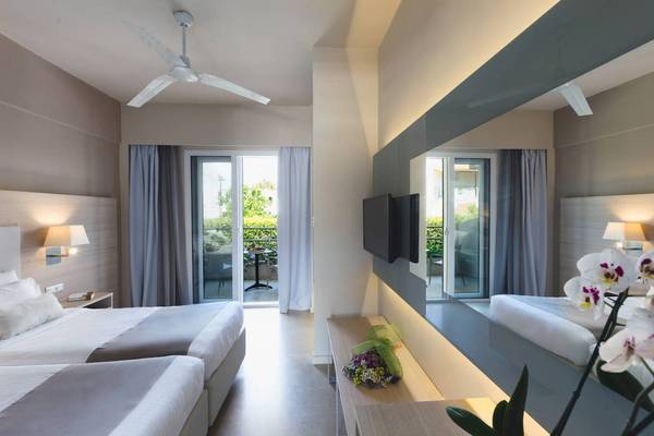 Innenansicht eines Hotelzimmers im Acharavi Beach Hotel mit drei Betten, einer Terrasse und einem Fernseher.