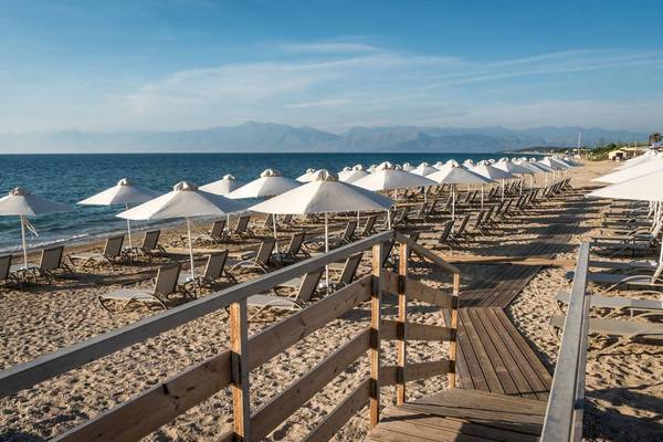 Strand des Acharavi Beach Hotels mit vielen Sonnenliegen und weißen Sonnenschirmen.