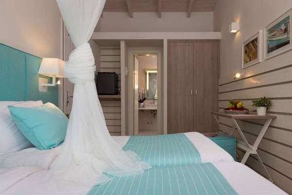 Doppelzimmer im Acharavi Beach Hotel mit zwei Betten, blauer Bettwäsche, Tisch, Pflanzen und Bildern an der Wand.