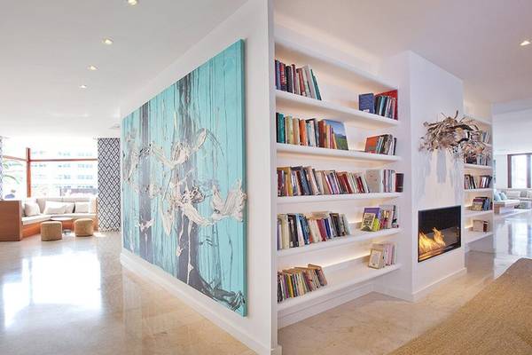 Innenbereich des HM Gran Fiesta Hotels mit einer großen Wandmalerei, Bücherregalen und einer Feuerstelle.