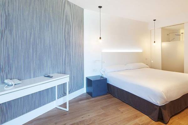 Ein elegantes Hotelzimmer im HM Gran Fiesta mit einem Bett, Nachttisch, Schreibtisch und modernen Lampen.
