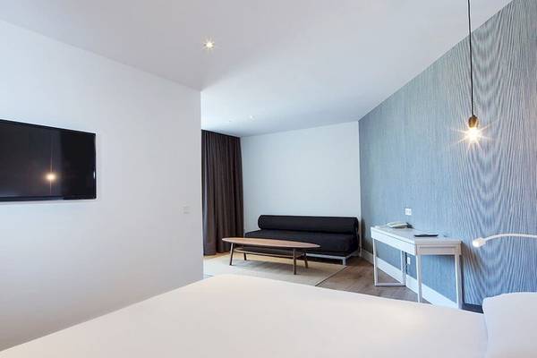 Ein modernes Hotelzimmer mit Fernseher an der Wand, Sofa und Schreibtisch.