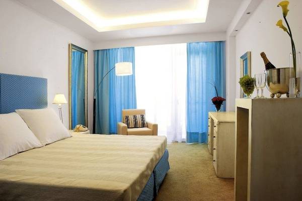 Schlafzimmer im Electra Palace Rhodes Hotel mit einem großen Bett, blauen Vorhängen und einem luxuriösen Ambiente.