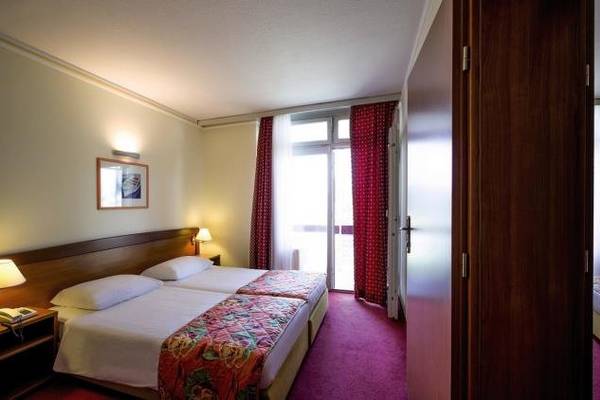 Innenansicht eines Doppelzimmers im Niko Hotel mit zwei Betten, Nachttischen und Lampen.