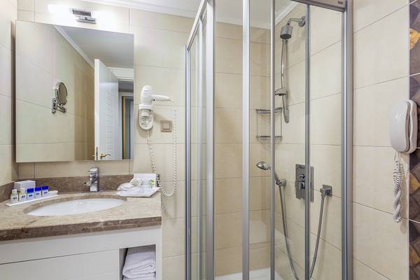 Hotel Badezimmer mit Spiegel, Föhn, Dusche und Waschbecken.