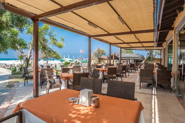 Außenbereich des Restaurants der Villa Side Residence mit Tischen und Stühlen, überdachter Terrasse und Blick auf den Strand