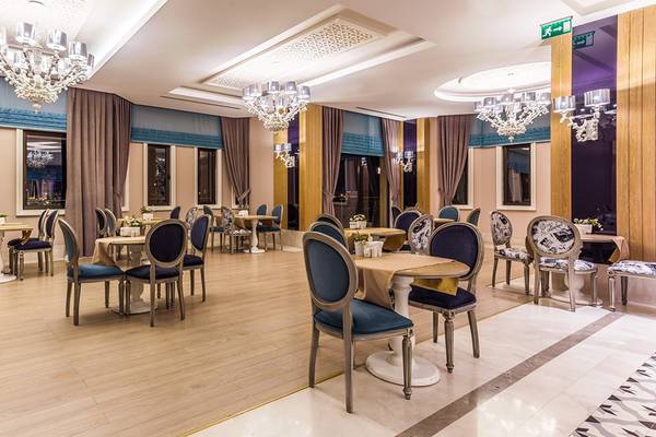 Innenansicht des Restaurants der Villa Side Residence mit Holzboden, blauen Stühlen und Tischen, Kronleuchtern und Vorhängen.