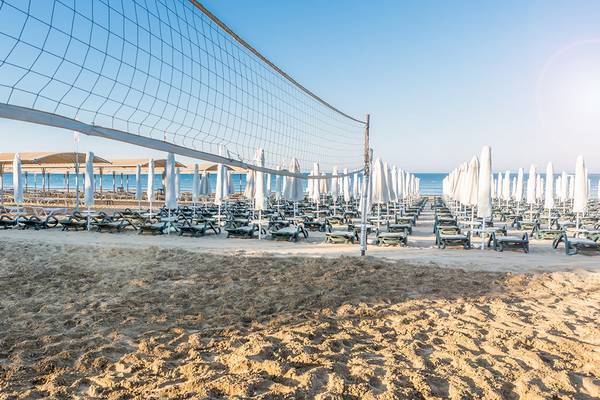 Strand mit Volleyballnetz und Sonnenliegen vor dem Meer