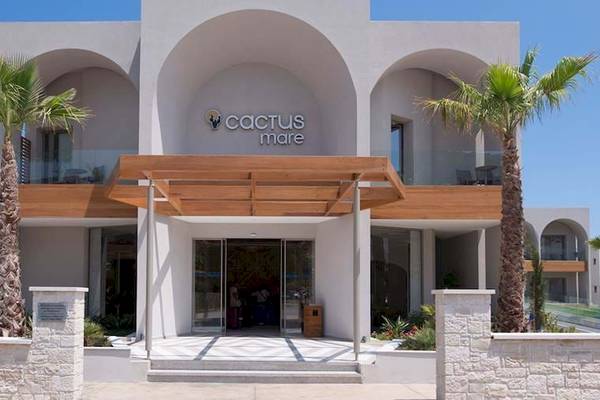Vorderansicht des Cactus Mare Hotels mit zwei Palmen und einem hölzernen Eingangsbereich