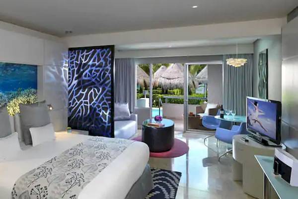 Hotelzimmer im Paradisus Playa del Carmen mit Meeresaquarium als Wandgestaltung, einem großen Bett, mehreren Kissen, und einem Fernseher.