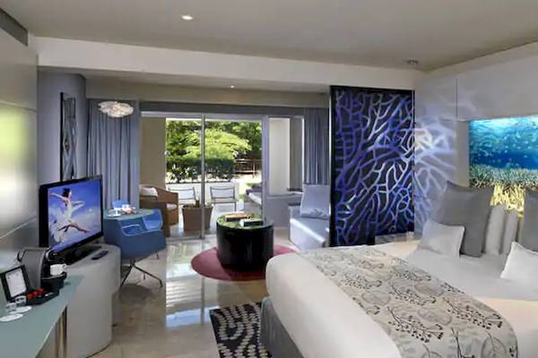Innenansicht eines Zimmers im Paradisus Playa del Carmen Hotel mit großem Bett, Fernseher, Möbeln und Aquarium-Wandbild.