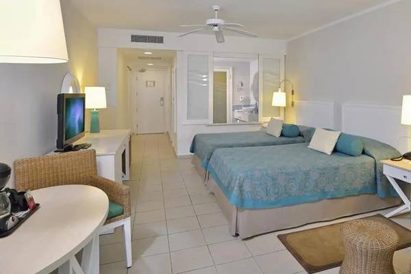 Doppelbettzimmer im Melia Marina Varadero Hotel mit zwei Betten, Fernseher, Tisch, Stühlen und Deckenventilator.