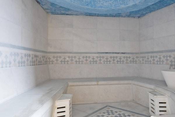 Saunaraum im Melia Athens Hotel mit weißen Wänden und Boden, blauen Akzenten und einer weißen Badewanne.