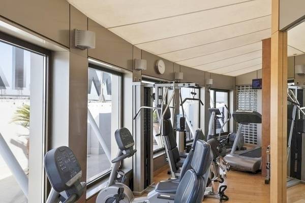 Fitnesscenter im Melia Athens Hotel mit verschiedenen Trainingsgeräten und großen Fenstern.
