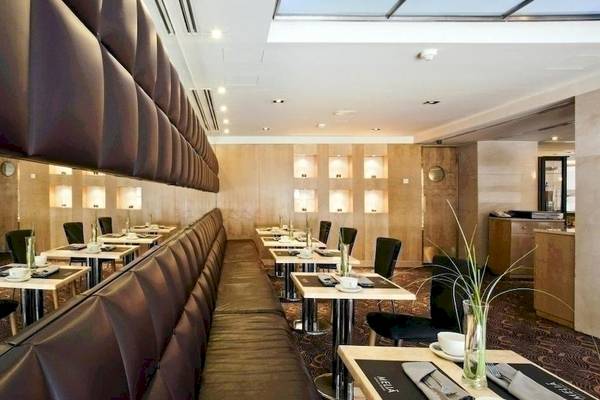 Innenansicht des Restaurants im Melia Athens Hotel mit Ledersesseln und Holztischen.