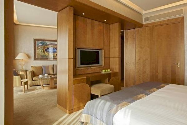 Innenansicht eines Hotelzimmers im Melia Athens mit Bett, Fernseher und Wohnzimmerecke.