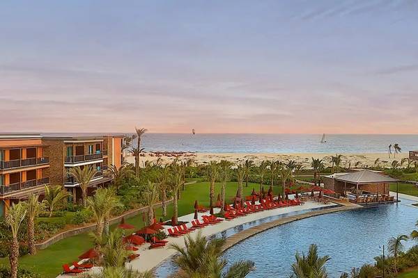 Außenansicht des Hilton Cabo Verde Sal Resorts mit Pool, Sonnenliegen und Palmen.