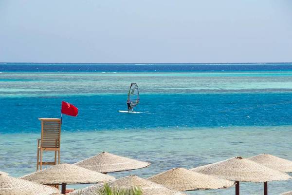 Windsurfer am Strand des Sea Star Beau Rivage Hotels mit Rettungsturm und Sonnenschirmen