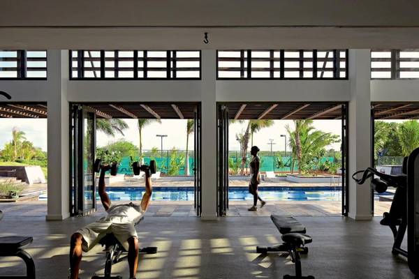 Fitnessstudio im Long Beach Mauritius mit einem Mann, der Hanteln hebt, und einem Pool im Hintergrund.