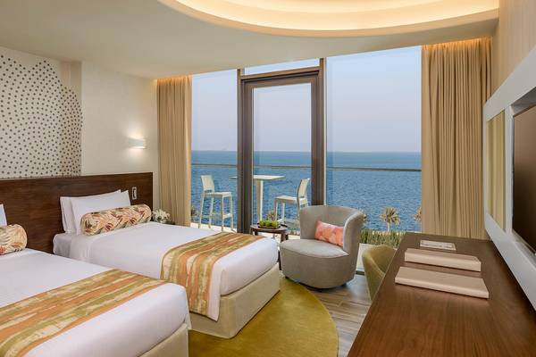 Suite-Zimmer mit Meerblick im Retreat Palm Dubai, zwei Betten, Schreibtisch und Balkon mit Tisch und Stühlen.