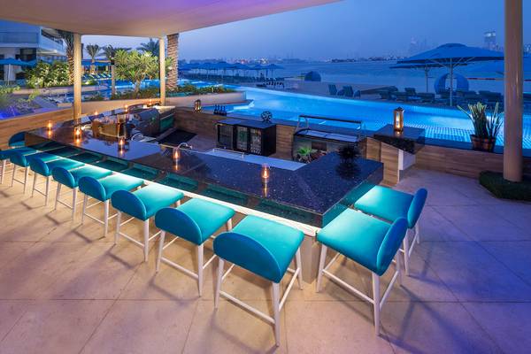 Außenbereich der Poolbar im The Retreat Palm Dubai MGallery mit blauen Stühlen und einem Blick auf den Pool und die Stadt.