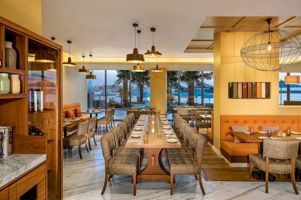 Innenansicht des Restaurants im Retreat Palm Dubai MGallery by Sofitel mit langer Tafel und Aussicht auf Palmen und Meer.
