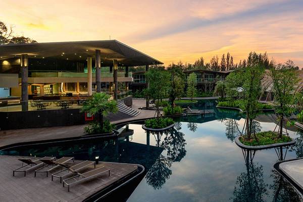 Außenansicht des Kalima Resort & Villas Khao Lak bei Sonnenuntergang mit Swimmingpool und Gebäuden.