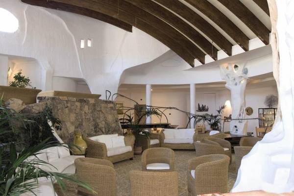Loungebereich im Baia Caddinas Hotel mit weißen Möbeln und braunen Korbstühlen.