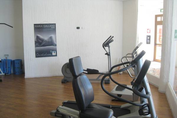 Fitnessbereich im Baia Caddinas Hotel mit mehreren Cardiogeräten und einer Plakatwand.
