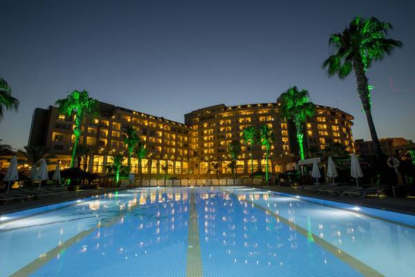 Die Außenansicht des Fame Residence Lara & Spa Hotels bei Nacht, mit beleuchteten Palmen und einem Pool.